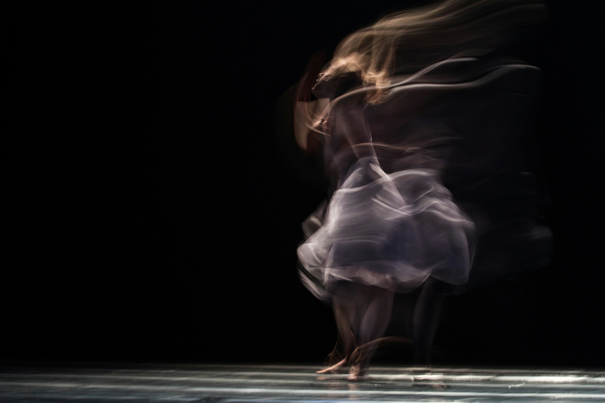 A dancer turning on a dark stage, with fabric tracing the movement.
