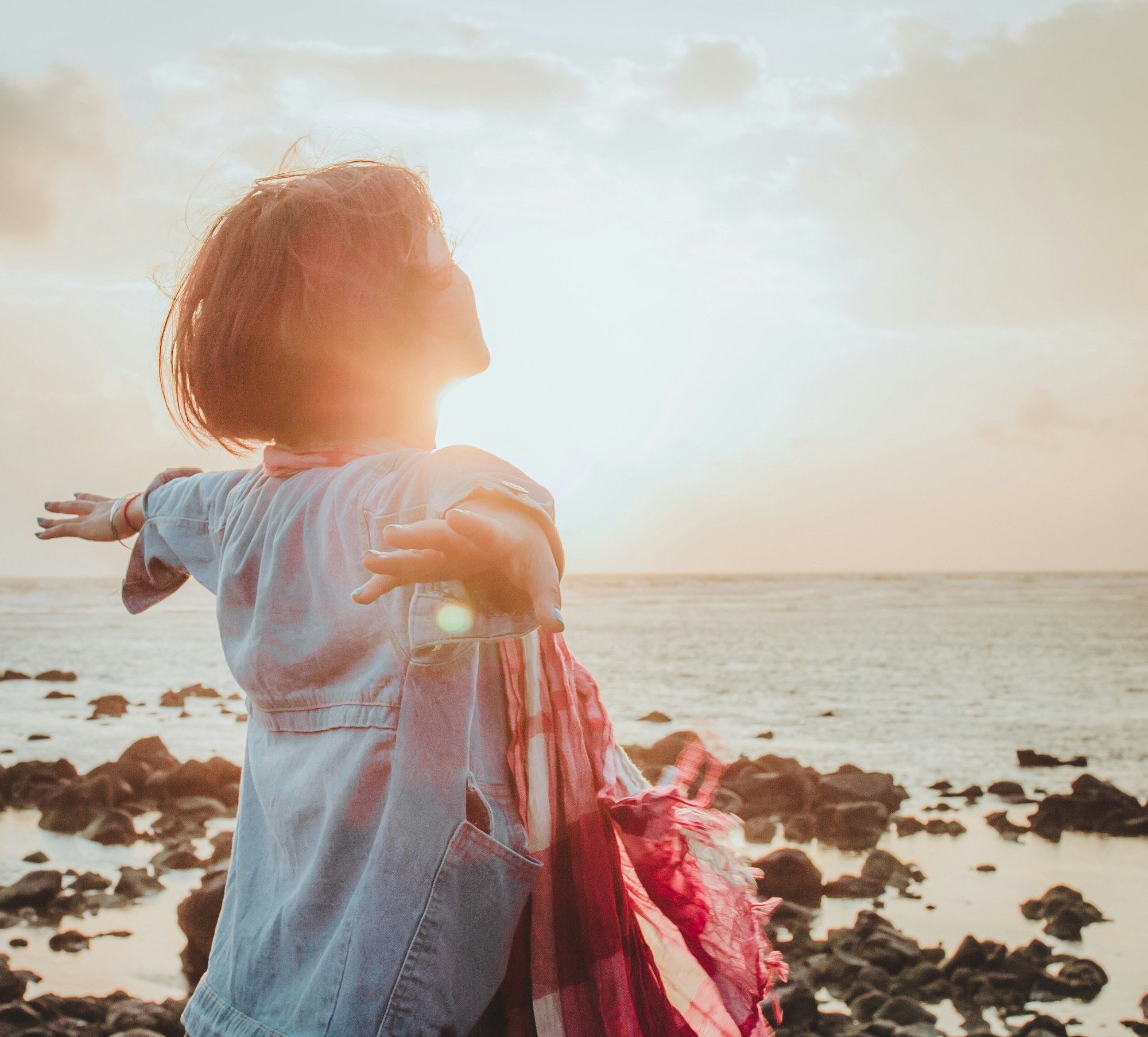 A young child reaching outward in the sunlight beside the sea.