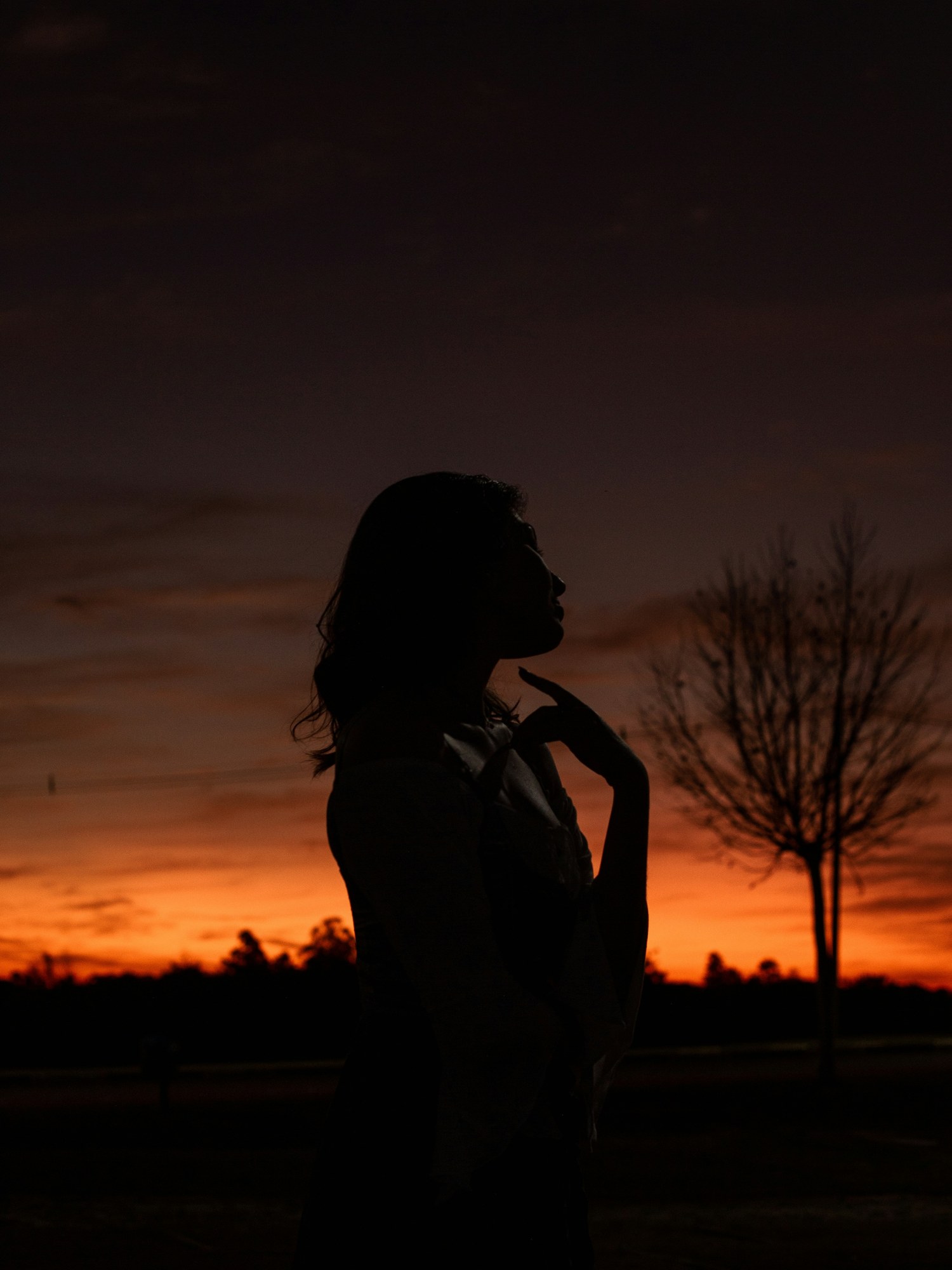 A woman in silhouette beneath an orange evening sky.
